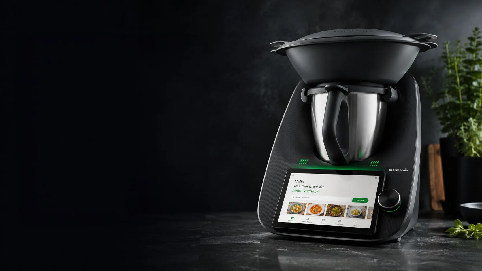 Thermomix TM7 mit aufgesetztem Varoma und eingeschaltetem Touchdisplay auf einer dunklen Küchenarbeitsplatte